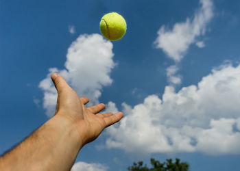 Cropped hand throwing tennis ball against sky