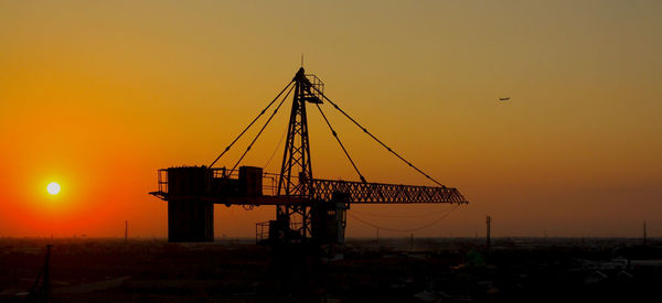 Silhouette cranes at construction site during sunset