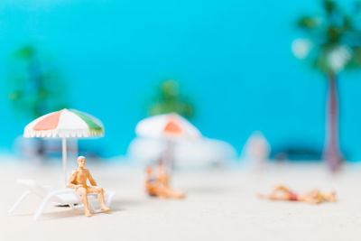 Miniature people wearing swimsuit relaxing on the beach with blue background