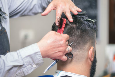 Cropped hands of barber cutting male customer hair in salon