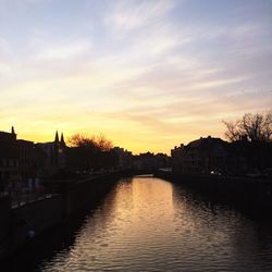 River in town against sky at sunset