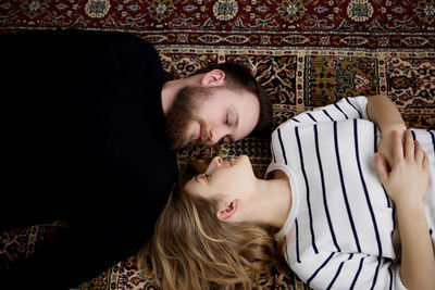 High angle view of couple looking at each other while lying on carpet at home
