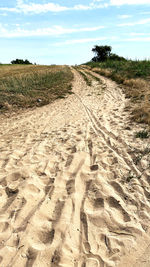 Tire tracks on sand land against sky