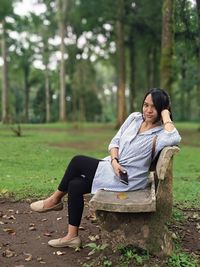 Full length portrait of woman sitting on bench at park