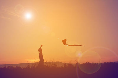 Silhouette girl flying kite on field against sky during sunset