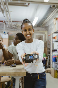 Portrait of smiling girl showing electric component in technology workshop at school