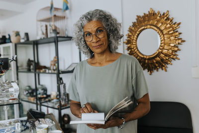 Portrait of confident female owner with diary standing in store
