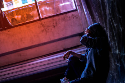 Side view of woman sitting against wall