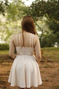 Rear view of young woman in dress standing on field at park