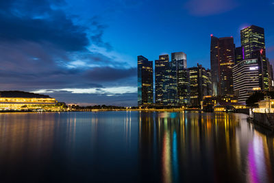 Illuminated buildings by sea against sky at night