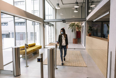 Businesswoman with protective face mask using id card at turnstile while entering office