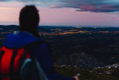 Rear view of woman looking at city against sky during sunset