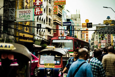 People walking by vehicles on street amidst buildings in city