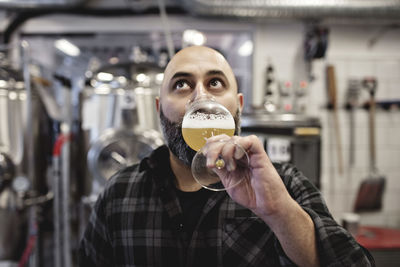 Male worker tasting craft beer while standing at factory