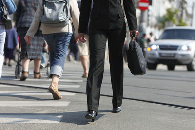 Low section of businesswoman holding bag while walking on city street
