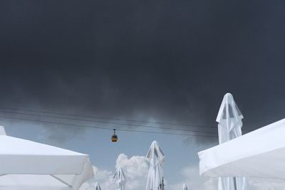 Low angle view of cable car over parasols against cloudy sky