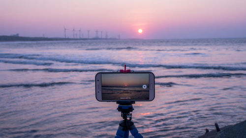 Close-up of camera on beach against sky during sunset