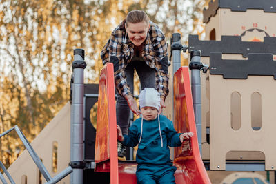 A boy, person with down syndrome walks in the park with his mother, going down the children's slide