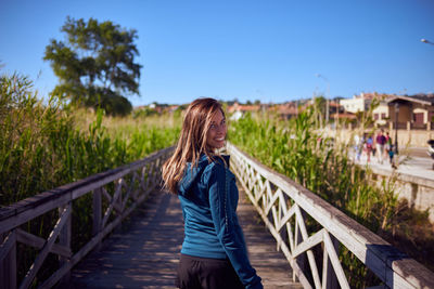 Woman standing on footbridge against blue sky