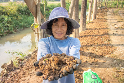 Portrait of smiling senior woman holding soil while standing at farm