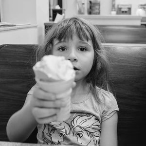 Portrait of girl having ice cream cone while sitting in restaurant