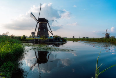 Traditional windmill by lake against sky