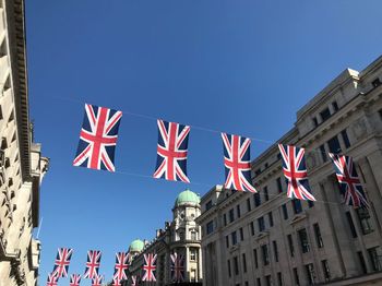 Low angle view of union jacks hanging in city against clear blue sky