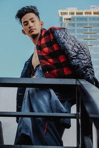 Young man looking away while standing on railing