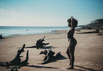 Full length of young woman standing on beach against clear sky