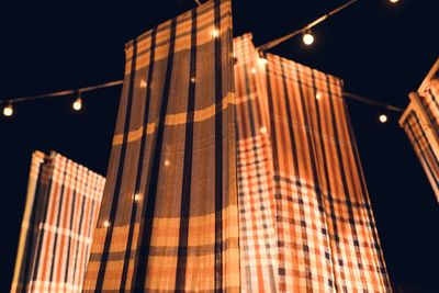 Low angle view of fabric hanging by illuminated lights against sky at night