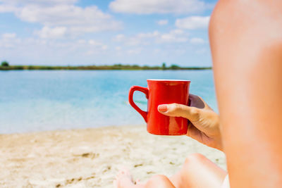 Midsection of woman drinking coffee on beach