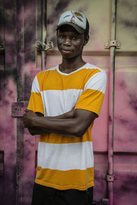 Young man wearing cap standing with arms crossed against container