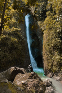 High angle view of man crouching on rock against waterfall