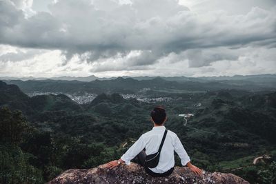 Rear view of man sitting on mountain against sky