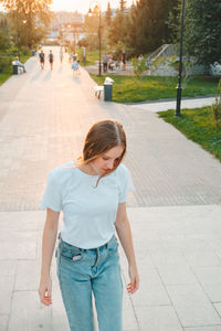 Red-haired teenager girl in a white t-shirt and jeans walks around the city. 