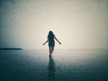 Rear view of woman walking in sea against cloudy sky