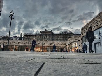 People walking on street amidst buildings in city against sky