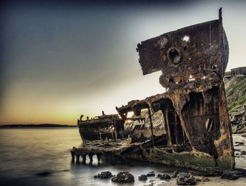 Abandoned ship in sea against sky during sunset