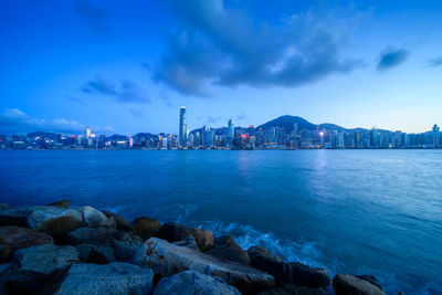 Sea by illuminated city buildings against sky