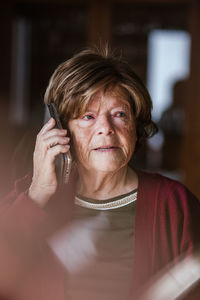 Elderly lady with wrinkled face looking away and answering phone call while being at home