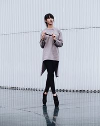 Full length portrait of young woman standing against wall