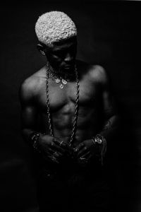 Close-up of shirtless man wearing jewelry against black background