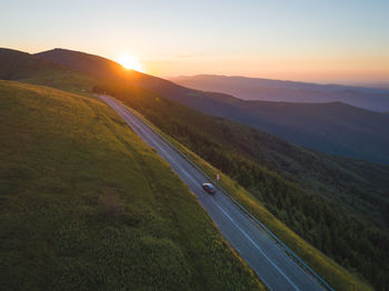 Scenic view of road amidst field against sky during sunset