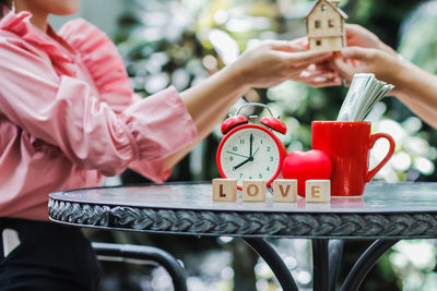 Midsection of girl holding model house with friend while sitting by table