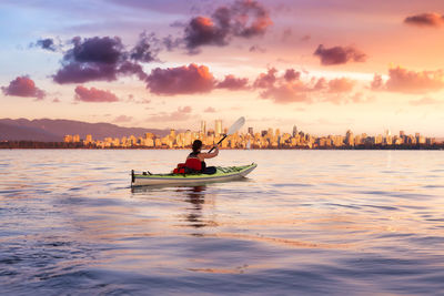 Man on boat in sea against sky during sunset