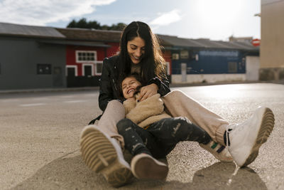 Cheerful mother and daughter playing while sitting on road