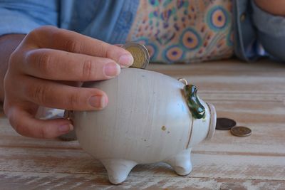 Midsection of woman inserting coin in piggy bank on table