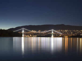 Illuminated bridge over river against sky at night