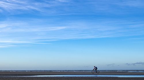 Man riding bicycle on road against sky