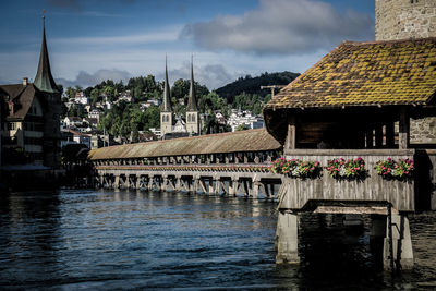 Bridge over river by buildings against sky